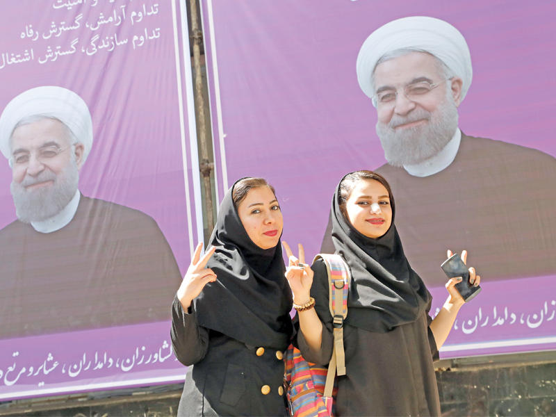 إيرانيتان بجوار لافتة دعائية لروحاني في مدينة كرج أمس (إي بي أيه)