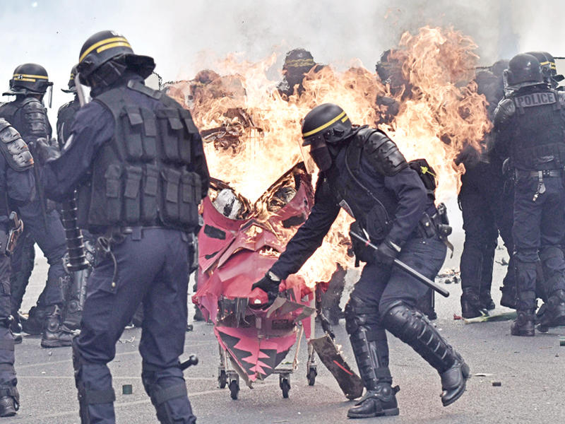 شرطي فرنسي يتصدى لعربة محترقة دفعها باتجاهه متظاهرون من اليسار الفوضوي في عيد العمال في باريس أمس (أ ف ب)