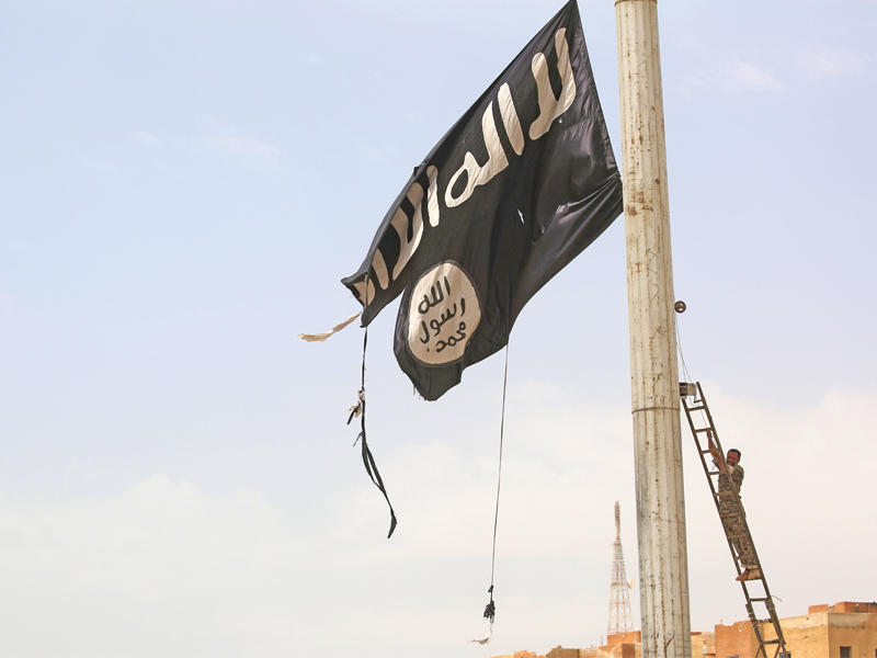 مقاتل في «قسد» يوشك أن ينزع راية لـ «داعش» في أحد أحياء مدينة الطبقة أمس الأول (أ ف ب)