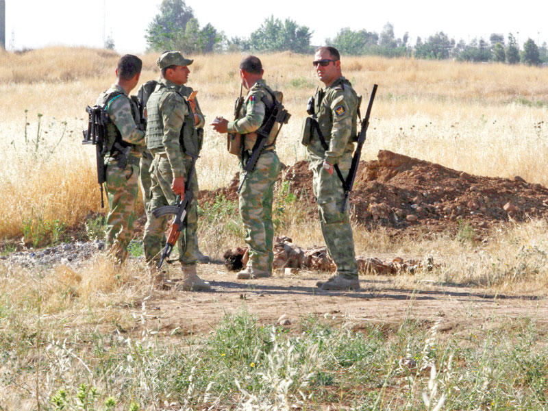 عناصر من البيشمركة تقف عند جثة أحد عناصر «داعش» الذين هاجموا قاعدة «كيه1» اليوم (رويترز) 