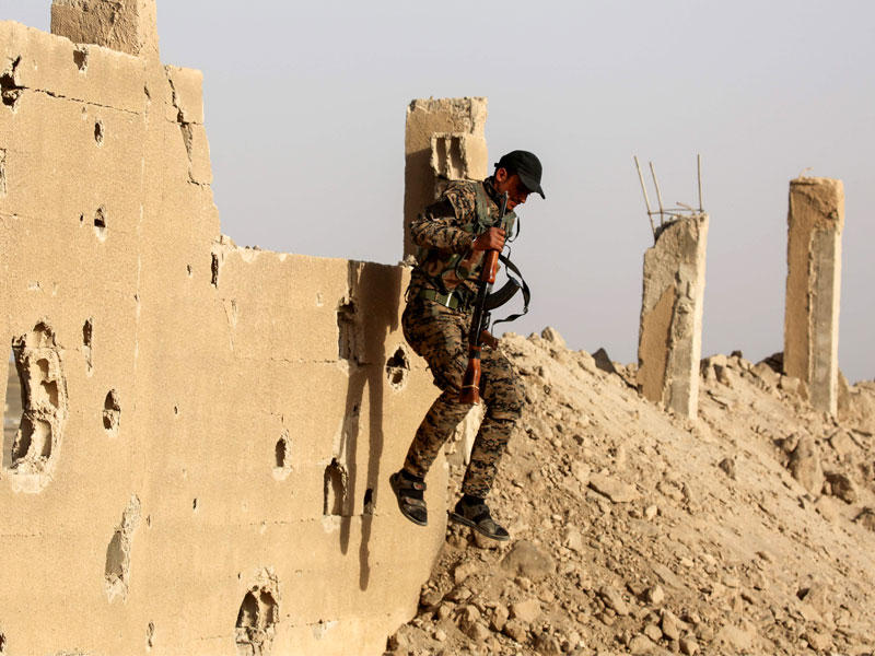 مقاتل كردي يقفز من أعلى جدار منزل مدمر في بلدة الكرامة بريف الرقة أمس الأول (أ ف ب)