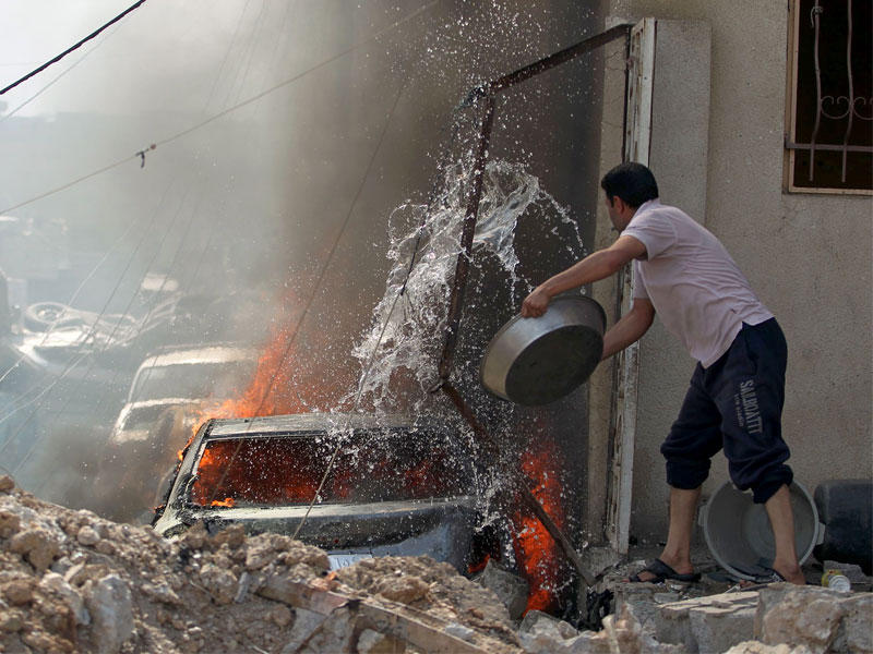 عراقي يحاول إطفاء النيران المشتعلة في سيارة بحي الرفاعي وسط الموصل أمس (أ ف ب)