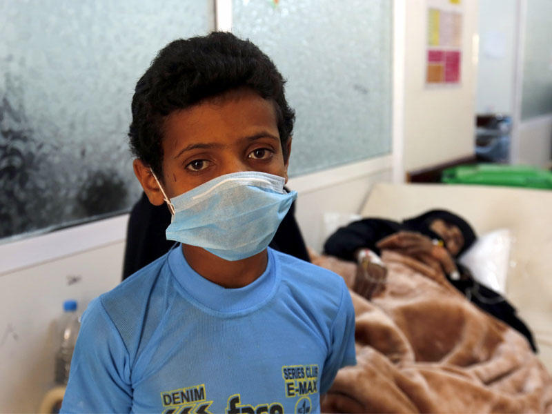 طفل يمني يرتدي قناعا يقف بالقرب من أمه المصابة بالكوليرا