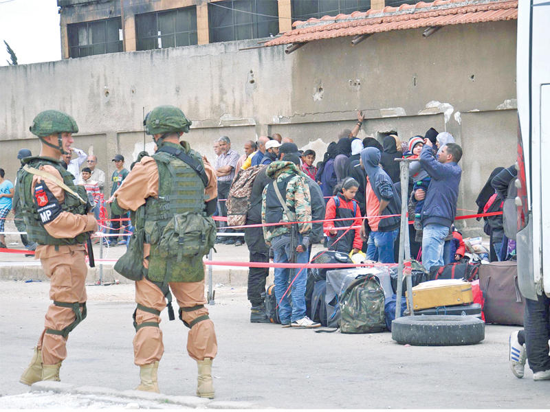 عنصران من القوات الروسية يتابعان عملية إجلاء مقاتلي المعارضة وأسرهم من حي الوعر بحمص أمس          (أ ف ب)