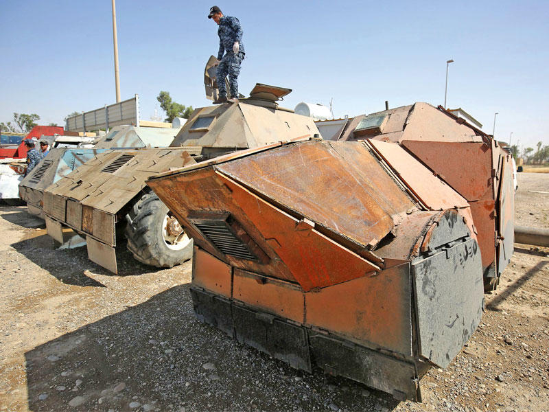 عنصر أمني أعلى سيارة مدرعة كانت بحوزة «داعش» في الجانب الأيمن من الموصل أمس (أ ف ب)