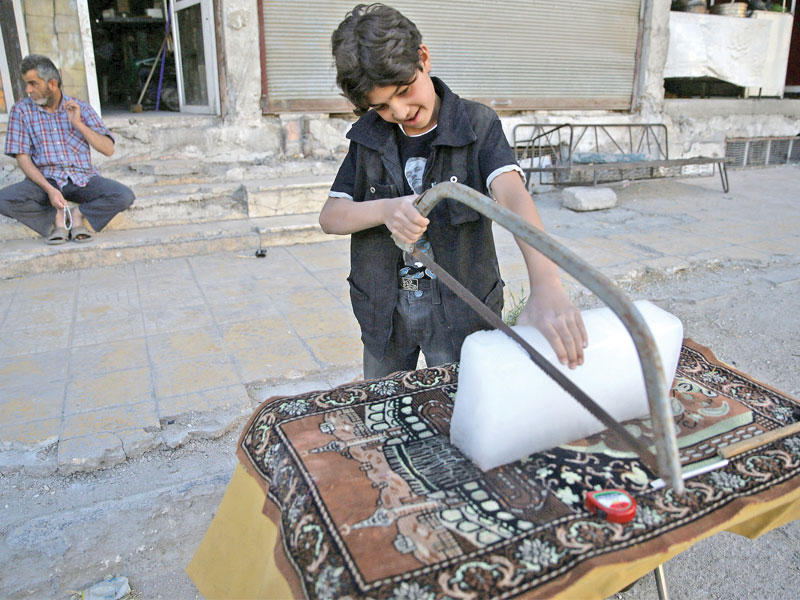 فتى سوري يقطع قالبا من الثلج في الغوطة الشرقية  المحاصرة أمس  (رويترز)