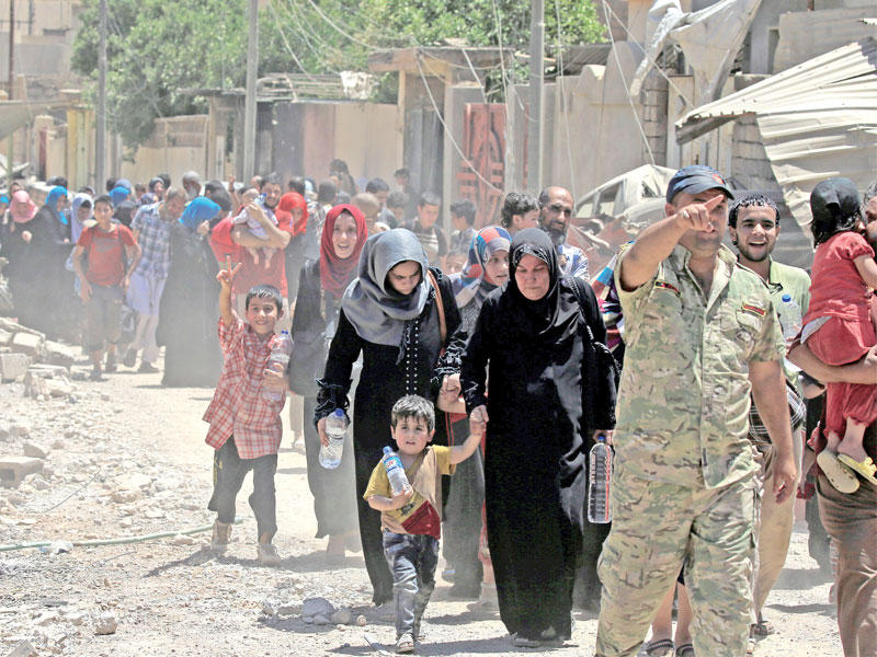 جندي عراقي يقود مدنيين فارين من القتال في حي الزنجيلي بوسط الموصل التاريخي أمس (رويترز)
