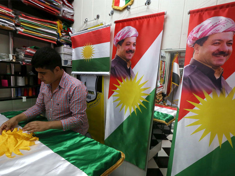 رجلا يخيط علم كردستان عراقي يحمل صورة لرئيس كردستان العراق مسعود بارزاني