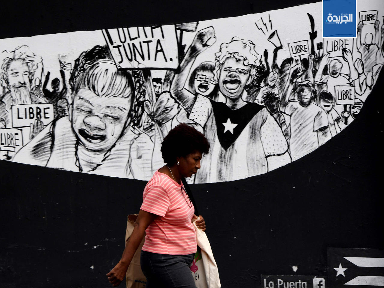 امرأة تسير على خلفية الجداريات الاحتجاجية في سان خوان، بورتوريكو