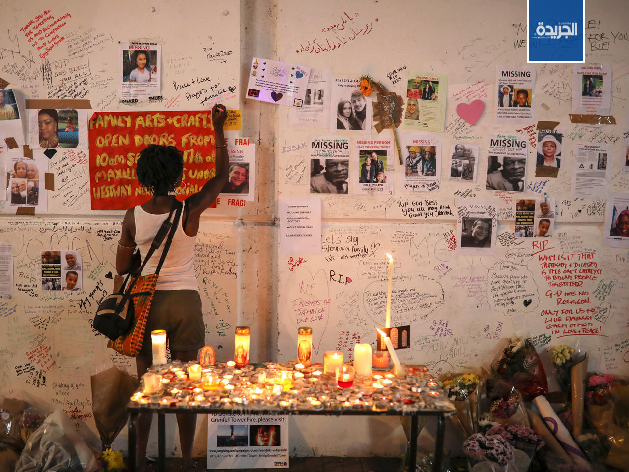 امرأة تكتب على رسالة للضحايا على جدار برج غرينفيل في شمال كنسينغتون، لندن