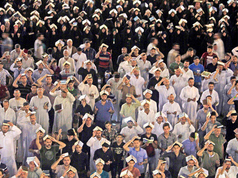 عراقيون شيعة يرفعون المصاحف على رؤوسهم في المسجد الكبير بالكوفة خلال إحياء دعاء رفع المصاحف مساء أمس الأول (أ ف ب)