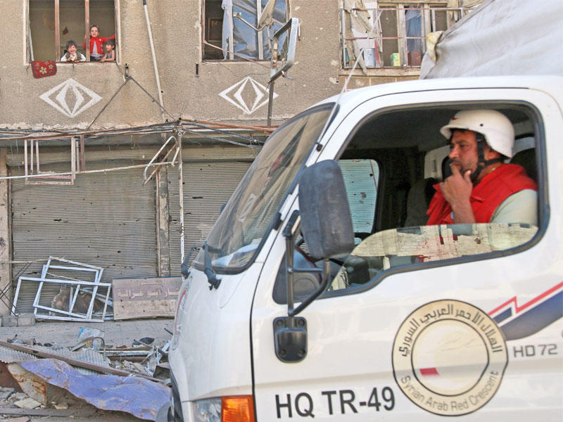 أطفال يتابعون من شرفة منزلهم المدمر دخول شحنة مساعدات لبلدة حراستا المحاصرة في الغوطة الشرقية أمس (أ ف ب)