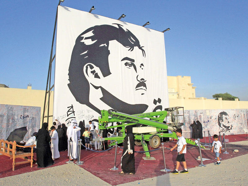 قطريون يتجمعون حول لوحة تصور الأمير تميم بن حمد في الدوحة اليوم (رويترز)