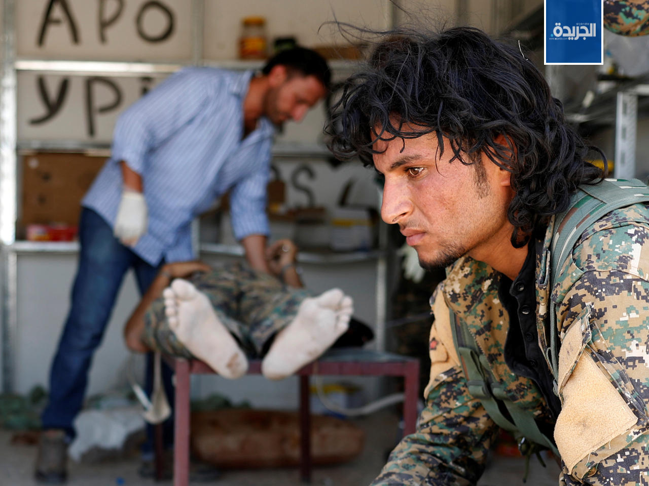 مقاتل من القوات الديمقراطية السورية ينتظر دوره بينما يقوم طبيب بمعالج رفيق مصاب