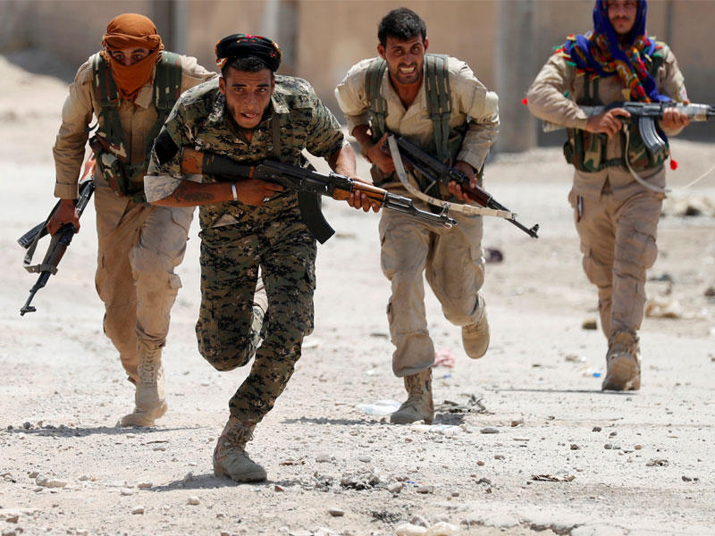 مقاتلون أكراد يعبرون شارعاً في الرقة أمس (رويترز)