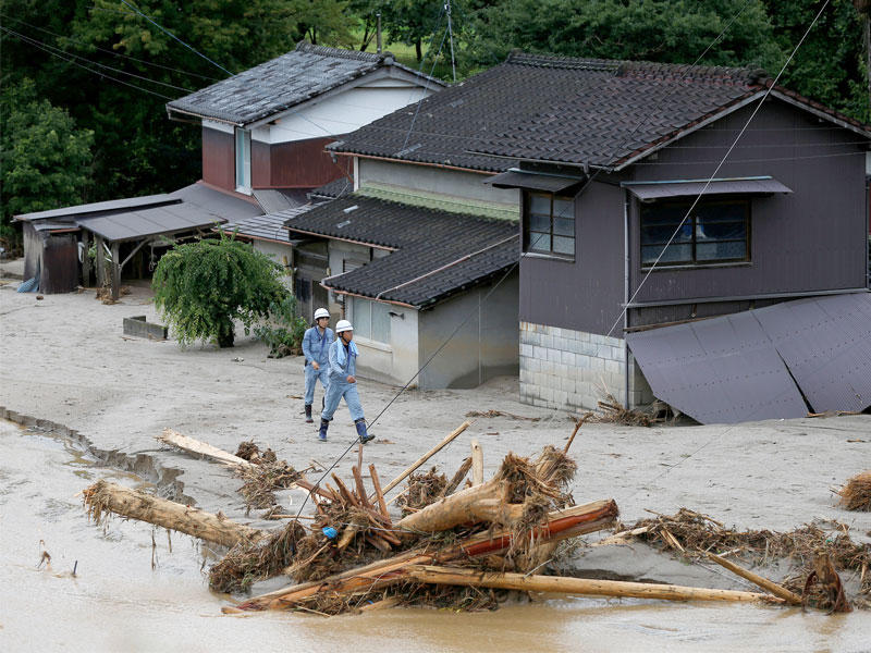 رجال يمشيون أمام المنازل المتضررة محاطة اجتاحت بعد هطول أمطار غزيرة في أساكورا