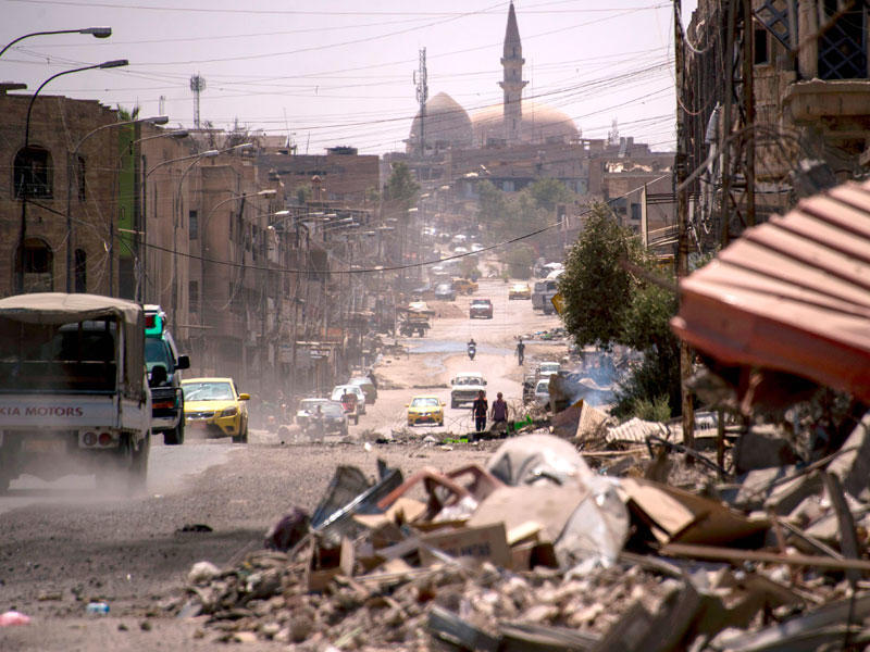 سيارات تسير في شارع طويل يظهر حجم الدمار في المباني على جانبيه في الموصل أمس الأول (أ ف ب)