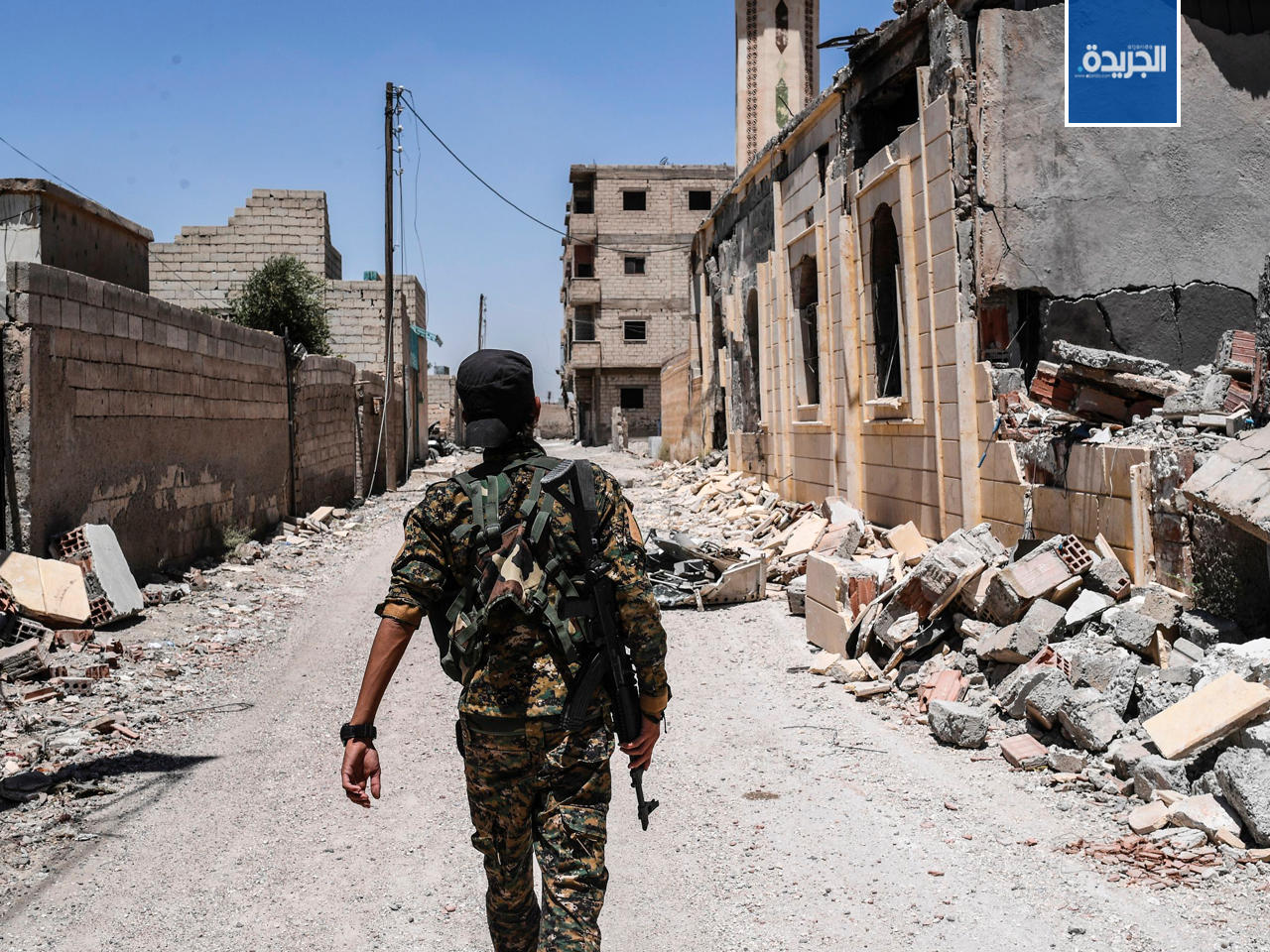 عنصر من القوات الديمقراطية السورية يمشي في شارع متضرر في الرقة الغربية