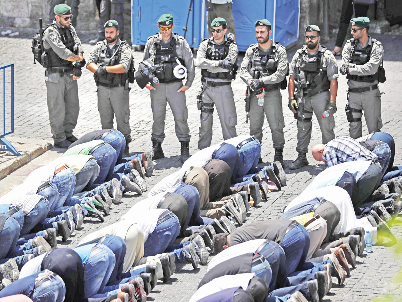 فلسطينيون يؤدون الصلاة أمس خارج المسجد الاقصى بالقدس تحت انظار الجنود الإسرائيليين (أ ف ب)