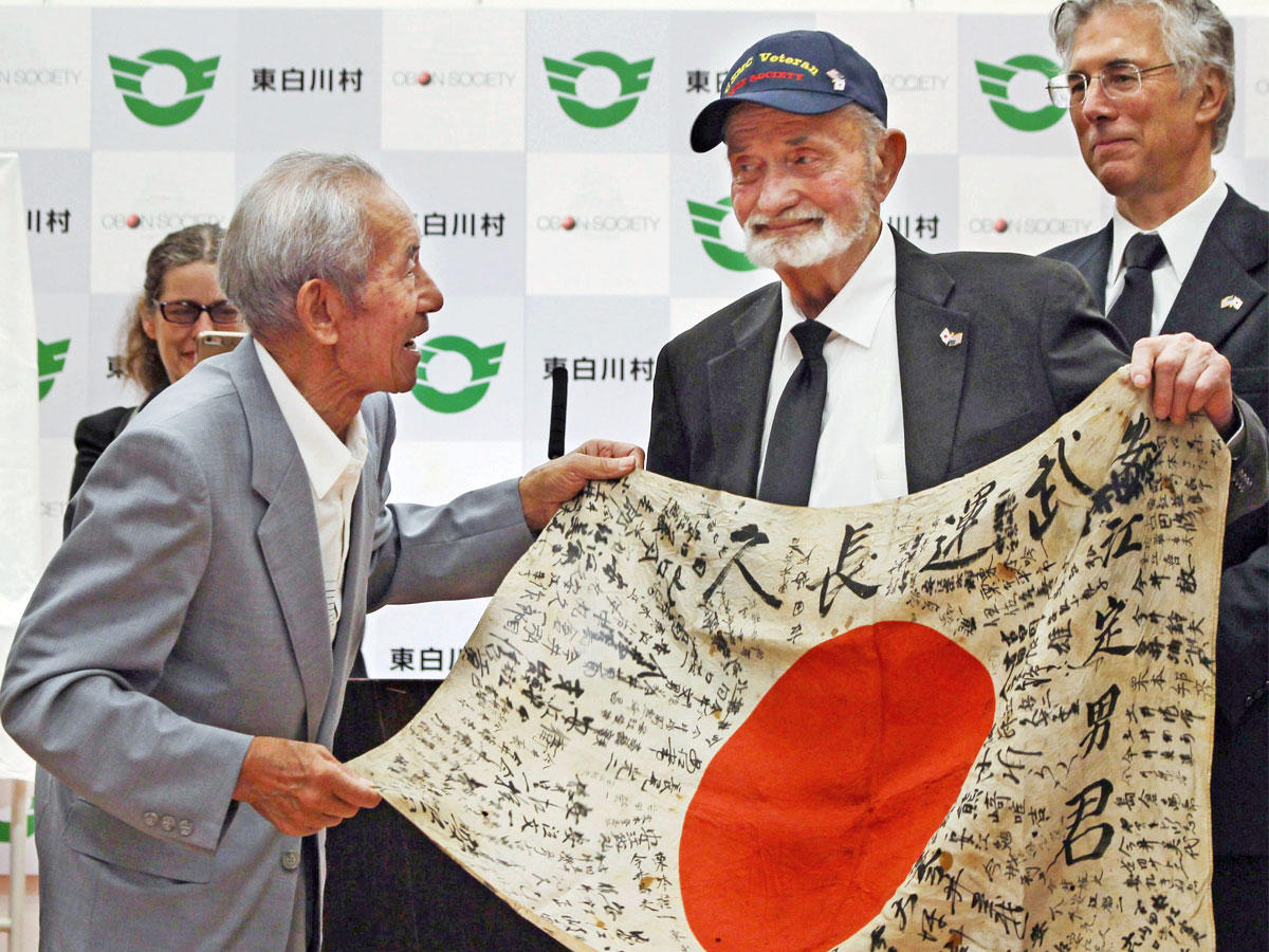 مارفين سترومبو الجندي بمشاة البحرية الأميركية سابقاً (وسط الصورة) يلتقي شقيق ساداو ياسو، الجندي الياباني الذي قتل في الحرب العالمية الثانية، ويسلم إليه علماً كان فوق الجثة، في صورة التقطت بقرية هيجاشي-شيراكاوا في اليابان