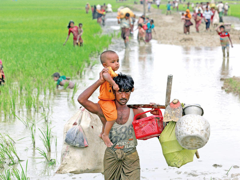لاجئ من الروهينغا يعبر بطفله حقل أرز نحو بنغلادش في تكناف أمس (رويترز)