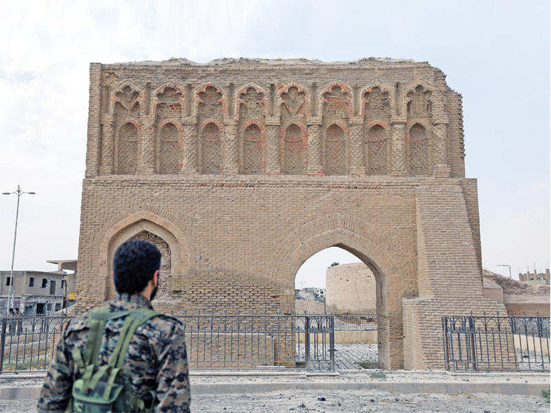 مقاتل من «قسد» يقف أمام بوابة بغداد في الرقة أمس (رويترز)