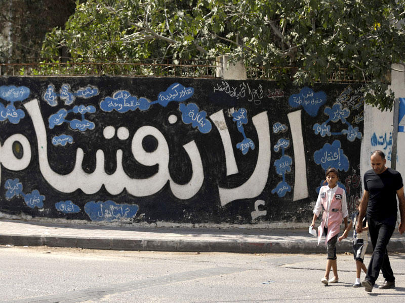 فلسطيني وابنتاه يمرون أمام رسم «غرافيتي» مناهض للانقسام وسط مدينة غزة أمس (أ ف ب)