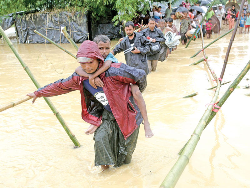 لاجئون روهينغا يعبرون جسراً بدائياً للهرب من مخيمهم الذي غرق بسبب الأمطار في بنغلادش أمس (اي بي ايه)