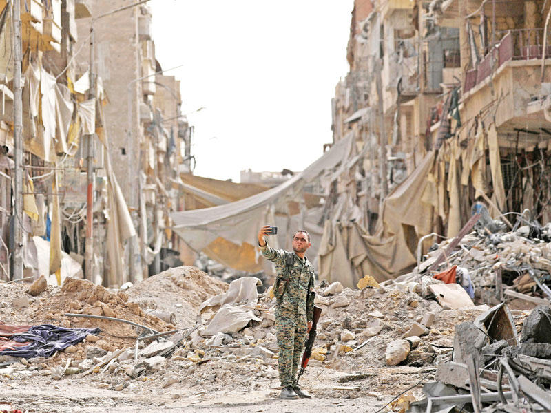 مقاتل من «قسد» يأخذ صورة سلفي وسط أنقاض الرقة أمس (رويترز)