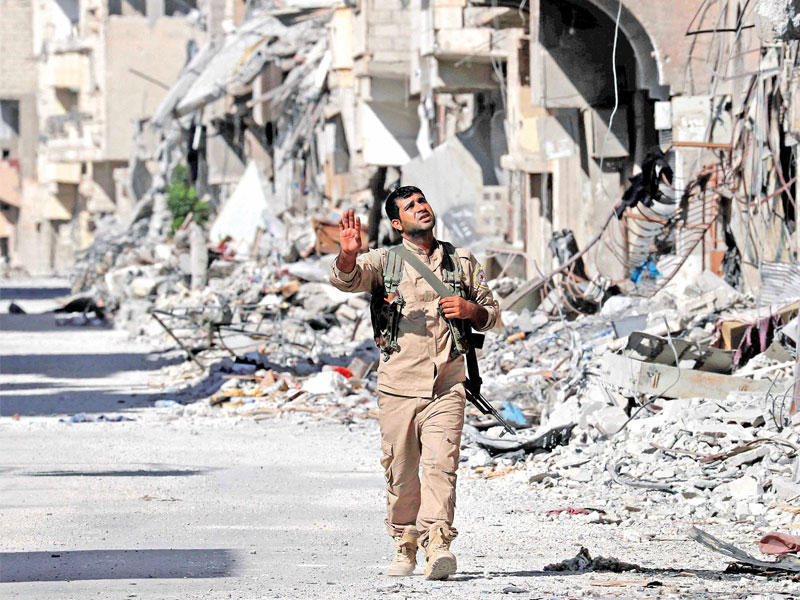 مقاتل كردي يمر بشارع مدمر في الرقة القديمة الأحد (رويترز)