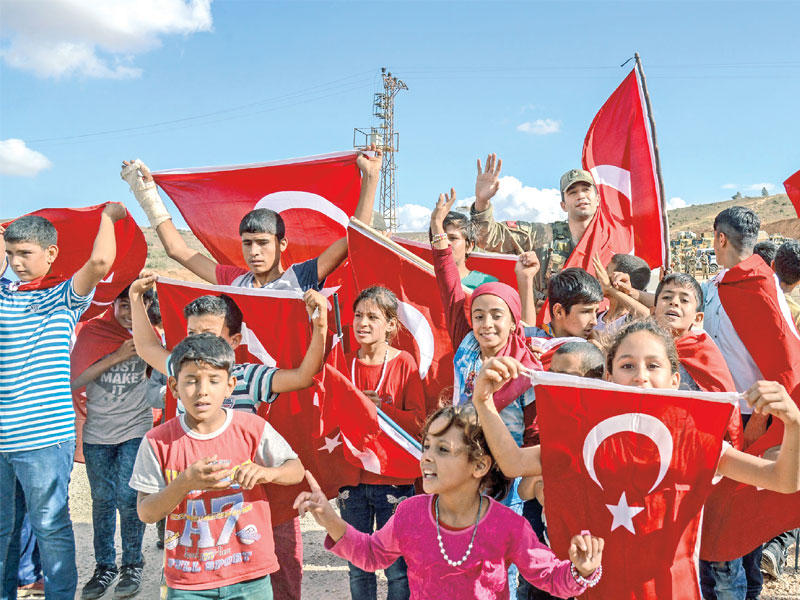 صبية سوريون مع جندي تركي يلوحون بأعلام تركيا دعماً لعملية إدلب بالقرب من الحدود  أمس الأول (أ ف ب)