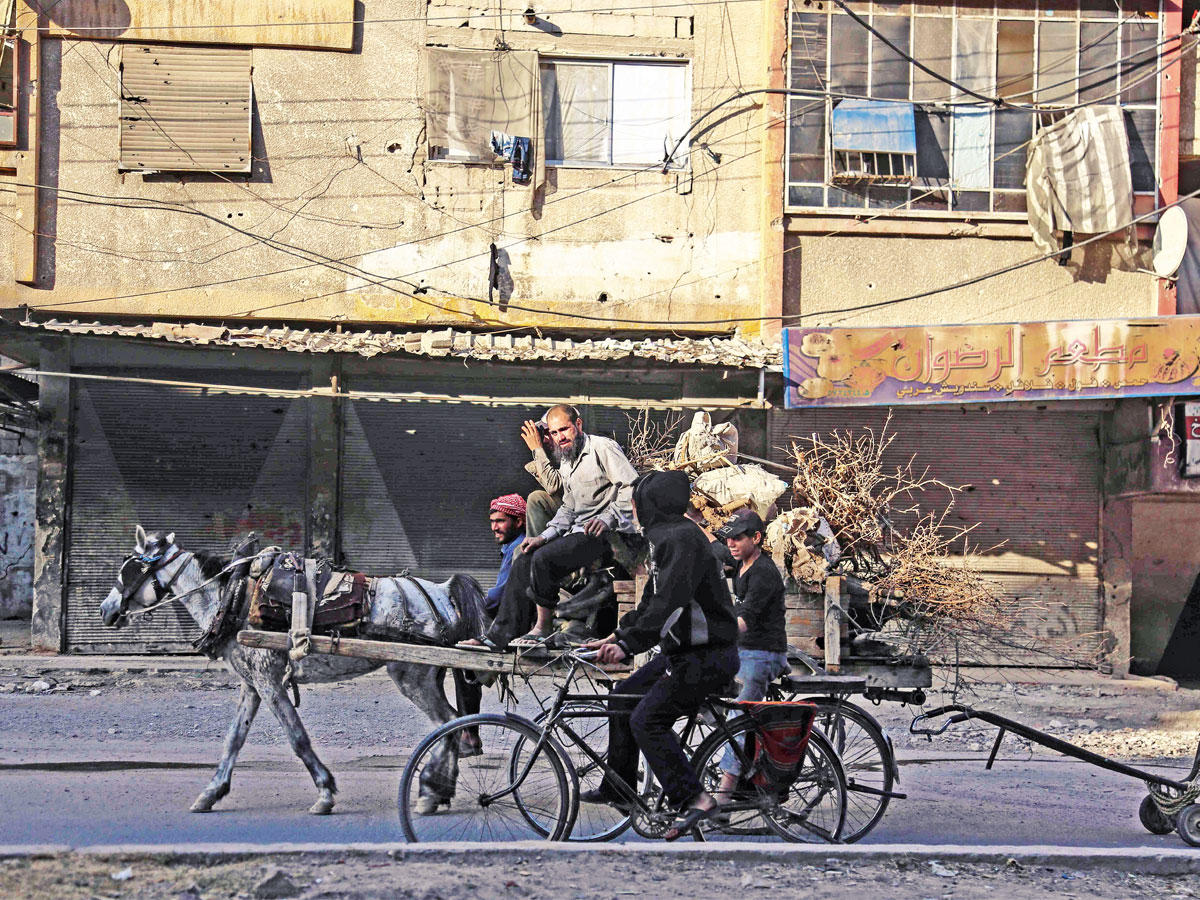 سوري ينقل أخشاباً على عربة يجرها حصان في حديث مع دراجين بدوما أمس الأول  (أ ف ب)