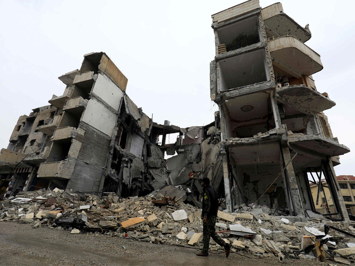 مقاتلا من القوات الديمقراطية السورية يعبر شارع مليء بالركام تحيط به المباني المتضررة في مدينة الرقة السورية