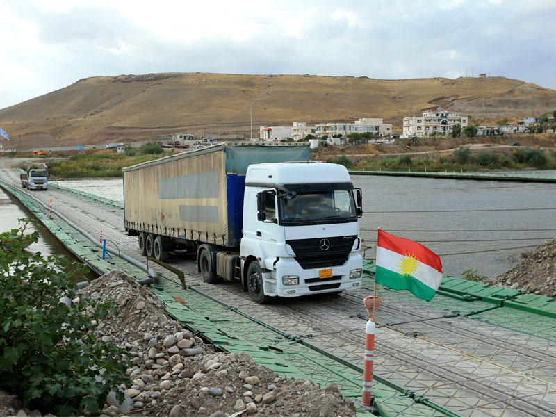 شاحنات تعبر معبر فيشخابور أمس ويبدو علم كردستان على الجسرt(رويترز)