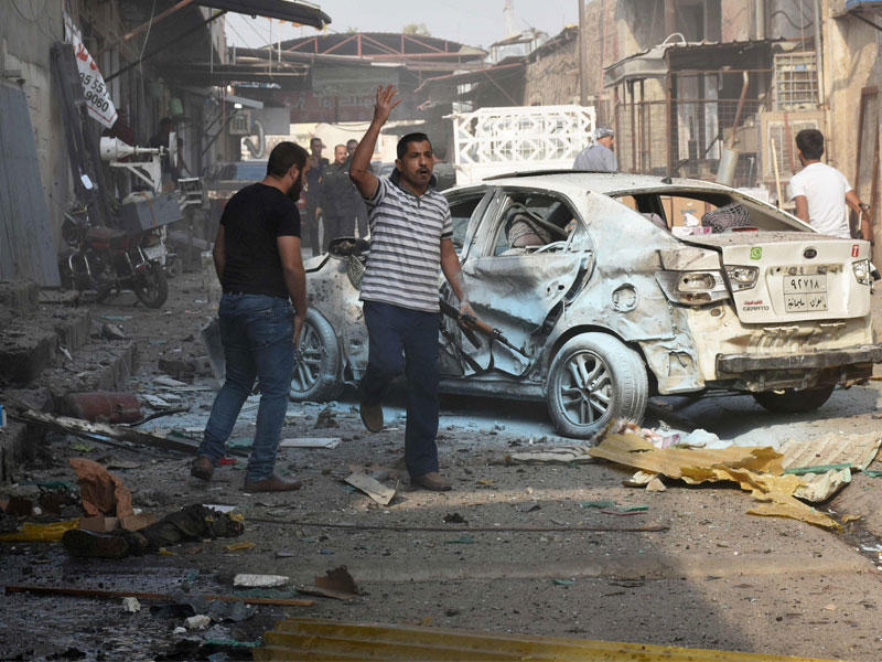 رجال عراقيون يقفون بجانب اشلاء وهم يفتشون مسرحا لهجوم انتحاري في منطقة التسوق في مدينة كركوك