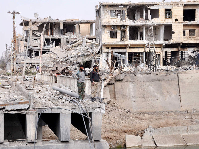 رجال يقفون على جسر متضرر في مدينة دير الزور شرق سوريا خلال عملية عسكرية شنتها القوات الحكومية