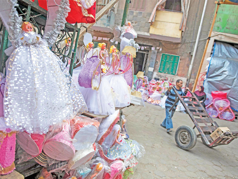 عامل بورشة لصناعة حلوى وعرائس «المولد النبوي» يدفع عربة بحي باب البحر وسط القاهرة أمس (إي بي إيه)