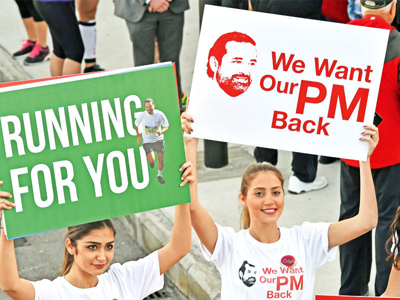 لبنانيتان ترفعان لافتتين تطالبان بعودة الحريري خلال ماراثون بيروت أمس  (إي بي أيه)