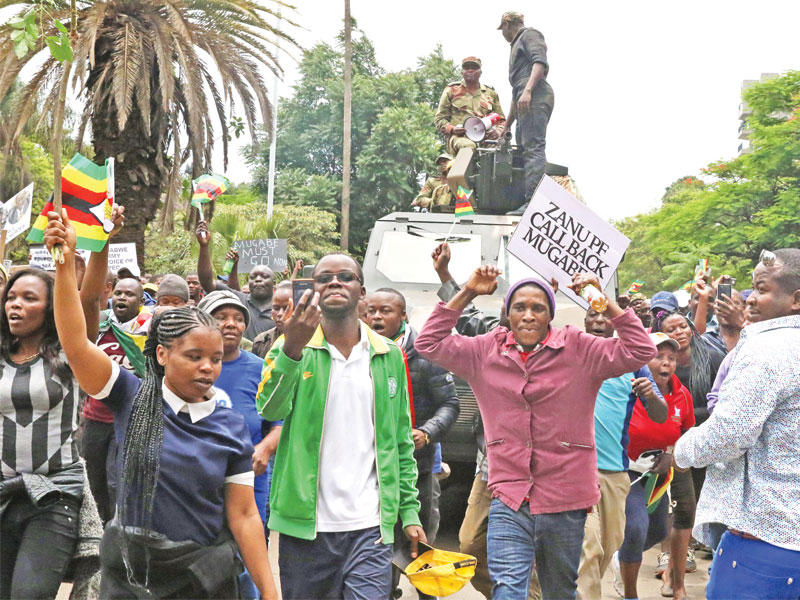 متظاهرون في حماية قوات من الجيش وسط هراري أمس يطالبون موغابي بالتنحي (رويترز)