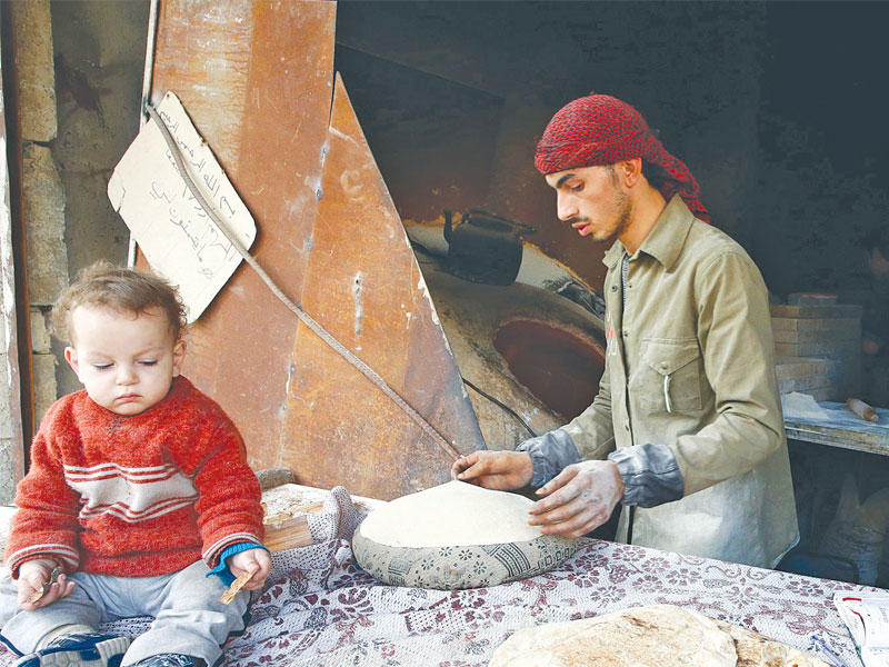 سوري يصنع الخبز في الحمورية بالغوطة الشرقية أمس الأول  (رويترز)