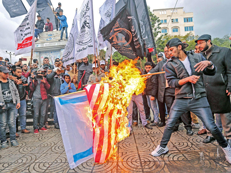  متظاهرون فلسطينيون يحرقون العلمين الأميركي والإسرائيلي في غزة أمس (أ ف ب)