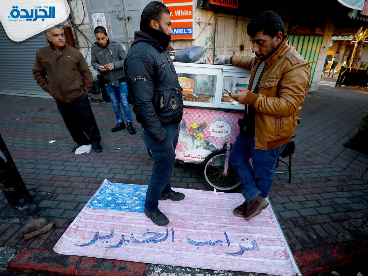 فلسطينيان يقفان على علم أمريكي كتب عليه «ترامب خنزير» في مدينة رام الله