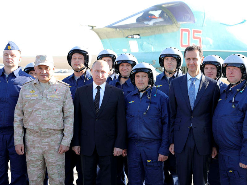 الرئيس الروسي فلاديمير بوتين وزير الدفاع سيرغي شويغو والرئيس السوري بشار الأسد مع الجنود أثناء زيارتهم لقاعدة هميميم الجوية في محافظة اللاذقية