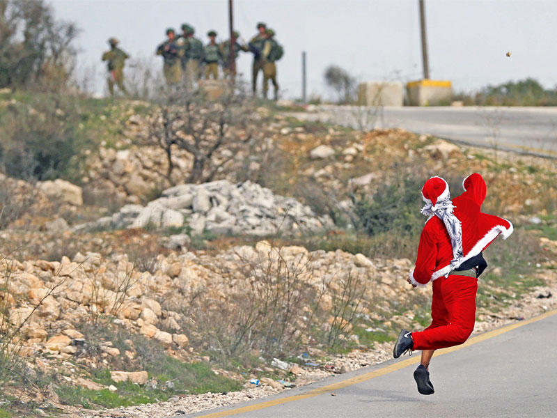 فلسطيني بملابس «سانتا كلوز» يرمي حجراً على قوة إسرائيلية خلال مواجهات أمس قرب رام الله في الضفة    (رويترز)