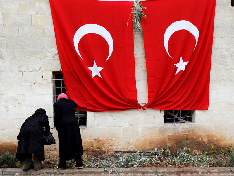 مسنان تركيان أمام علمين تركيين رفعا على مسجد تعرض لصاروخ في مدينة كيليس التركية الحدودية مع سورية مما أدى إلى مقتل 3 (رويترز)n