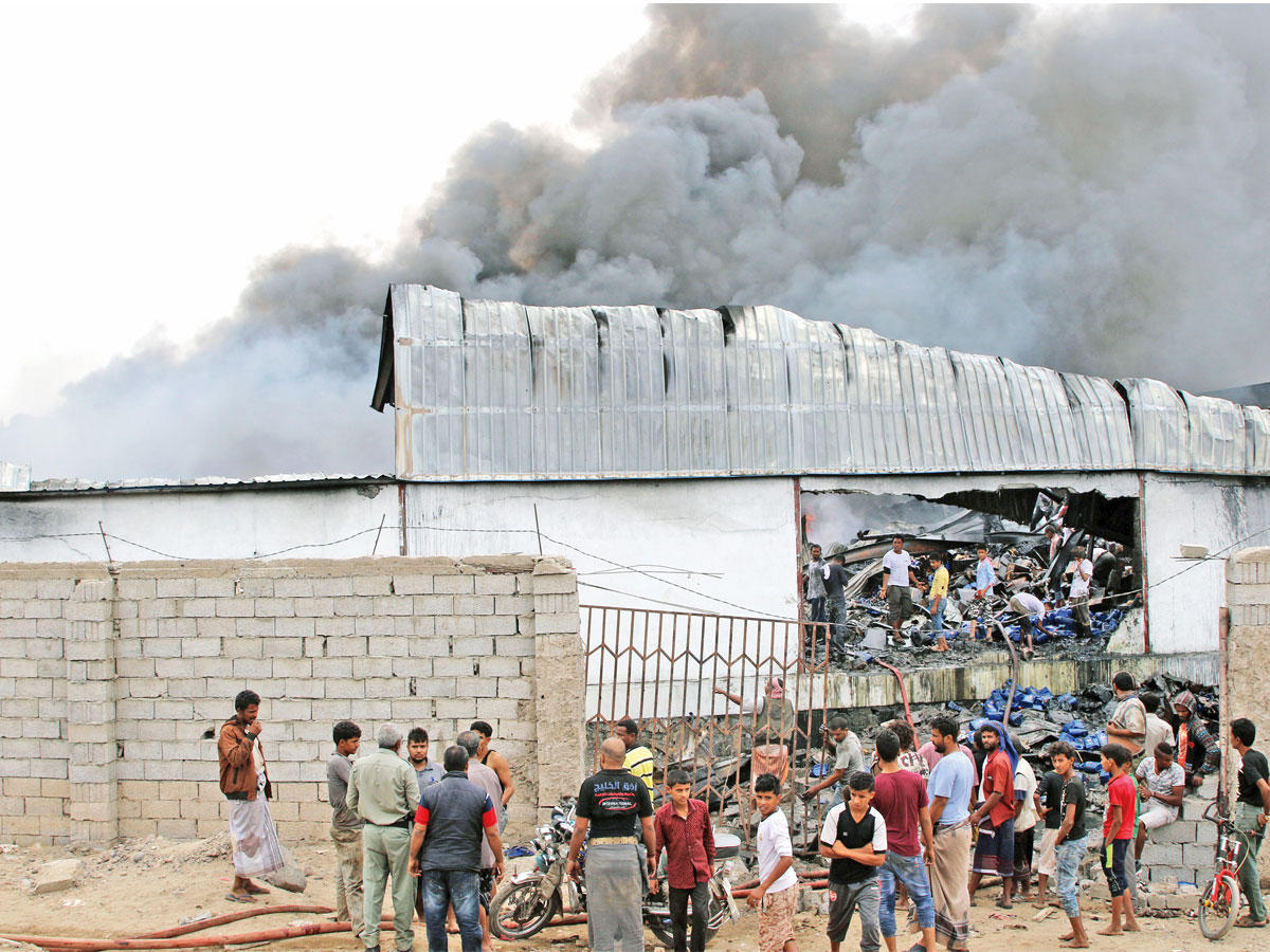 يمنيون يتفقدون مخزناً تعرض لقذيفة من جراء الاشتباكات في عدن أمس (رويترز)