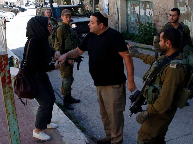 مستوطن إسرائيلي يواجه مراسلة فلسطينية قرب جيب استيطاني في الخليل أمس (أ ف ب) 