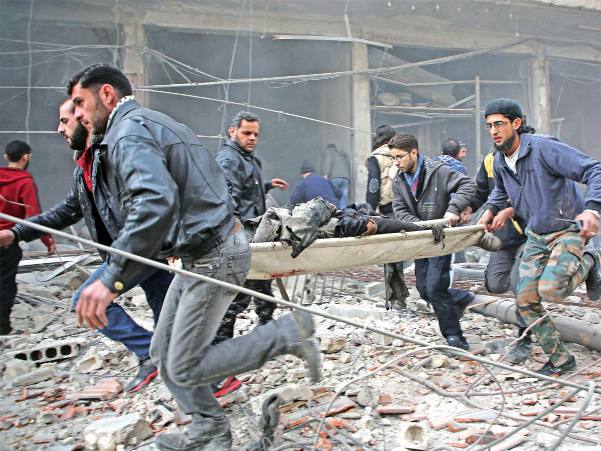 سوريون يجلون مصاباً تحت القصف في كفر بطنا بضاحية الغوطة المحاصرة أمس (أ ف ب)