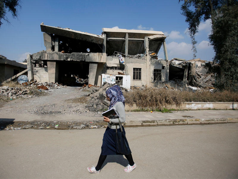طالبة تسير أمام جامعة الموصل المدمرة أمس  (رويترز)