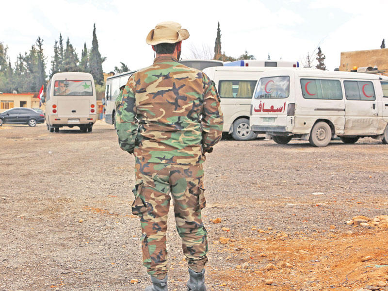 جندي للنظام مع حافلات وسيارات إسعاف تنتظر خروج مدنيين من الغوطة على حاجز الفاقدين على أطراف دمشق أمس (أ ف ب)